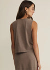 Woman wearing a brown sleeveless top and skirt set against a beige background