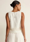 Woman wearing a white sleeveless top with lace details on a beige background