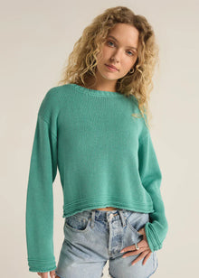  Woman wearing a teal sweater and denim shorts on a plain background