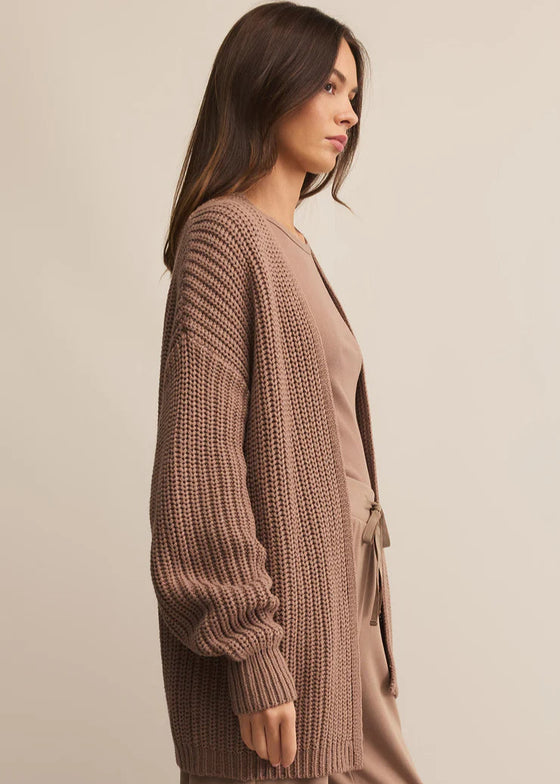 Woman wearing a brown knitted cardigan and pants on a beige background