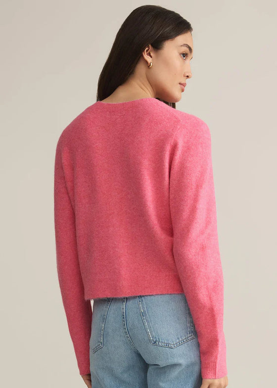 Person wearing a pink sweater and blue jeans against a plain background
