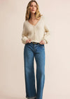 Woman wearing a cream cardigan and blue jeans on a beige background