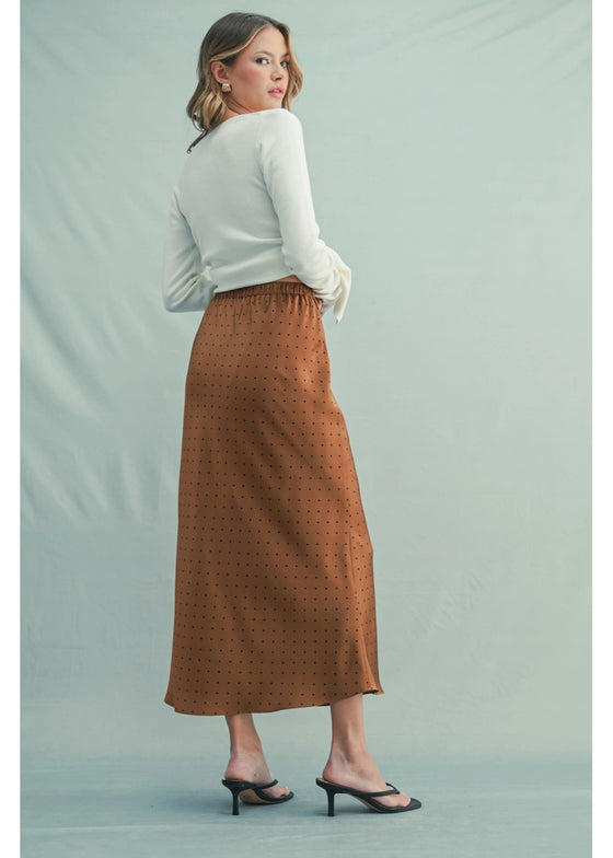 Woman wearing a white top and brown patterned skirt on a light green background