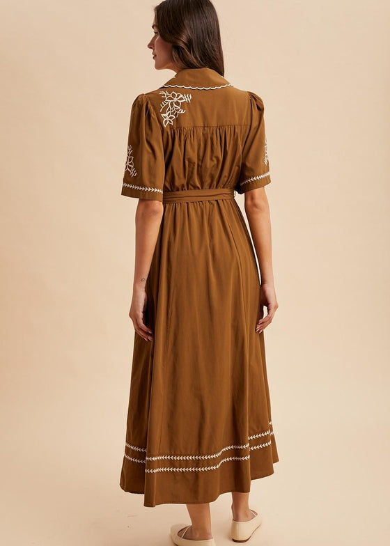 Woman wearing a brown dress with white embroidery on a beige background
