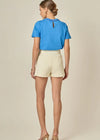 Woman wearing a blue top and beige shorts on a plain background