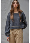 Woman wearing a dark blue sweater and beige pants against a gray background