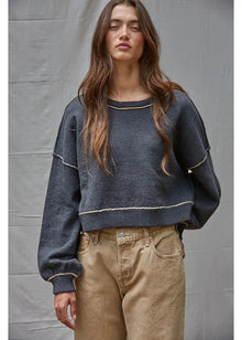  Woman wearing a dark blue sweater and beige pants against a gray background