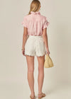 Woman wearing a pink blouse and white shorts with a beige background