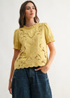 Woman wearing a yellow lace top and blue jeans against a white background