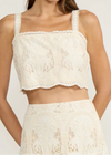 Woman wearing a cream lace top and skirt set against a white background