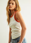 Woman wearing a white tank top with red trim and blue jeans against a plain background