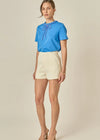 Woman wearing a blue blouse and beige shorts on a plain background