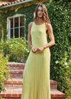 Woman in a yellow dress standing outdoors with greenery and a building in the background