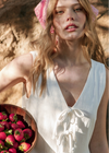 Woman in a white dress holding a bowl of strawberries outdoors.