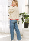 Woman wearing a cream sweater and blue jeans standing indoors with a plant in the background