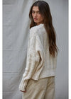 Woman wearing a textured beige sweater and pants against a plain background