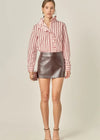 Woman wearing a pink and white striped blouse with a black leather skirt on a beige background