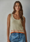Woman wearing a beige ribbed tank top with orange trim and blue jeans against a gray background