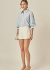 Woman wearing a light blue striped shirt and white skirt on a beige background