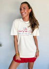 Woman wearing a white t-shirt with a graphic design and a red skirt against a light blue wall.