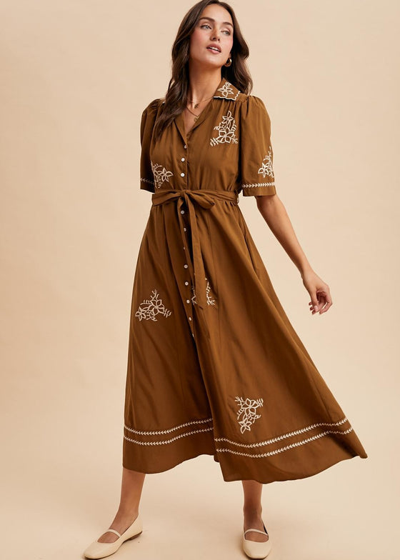 Woman wearing a brown dress with white embroidery on a beige background