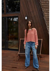 Woman in a striped sweater and blue jeans standing on a wooden deck with a wooden building in the background.