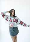 Person wearing a white sweatshirt with 'Oklahoma' printed on it, standing against a white background.