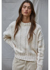 Woman wearing a cream knitted sweater against a plain background