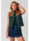 A woman models a sleeveless quilted vest with dark green body panels and brown leather-look shoulder yokes, worn over a black top and paired with a denim skirt against a light gray studio background.