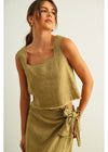 Woman wearing a green sleeveless top and skirt set against a light background