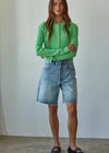 Woman wearing a green sweater and denim shorts against a plain background