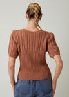 Person wearing a brown knitted sweater and blue jeans on a plain background