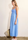 Woman wearing a blue dress standing on sand with a white wall background