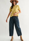Woman wearing a yellow top, blue jeans, and tan boots on a white background