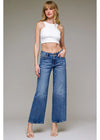 Woman wearing a white crop top and blue jeans against a plain background