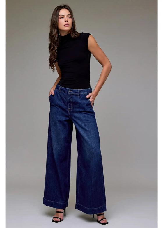 Woman wearing a black sleeveless top and blue wide-leg jeans against a gray background