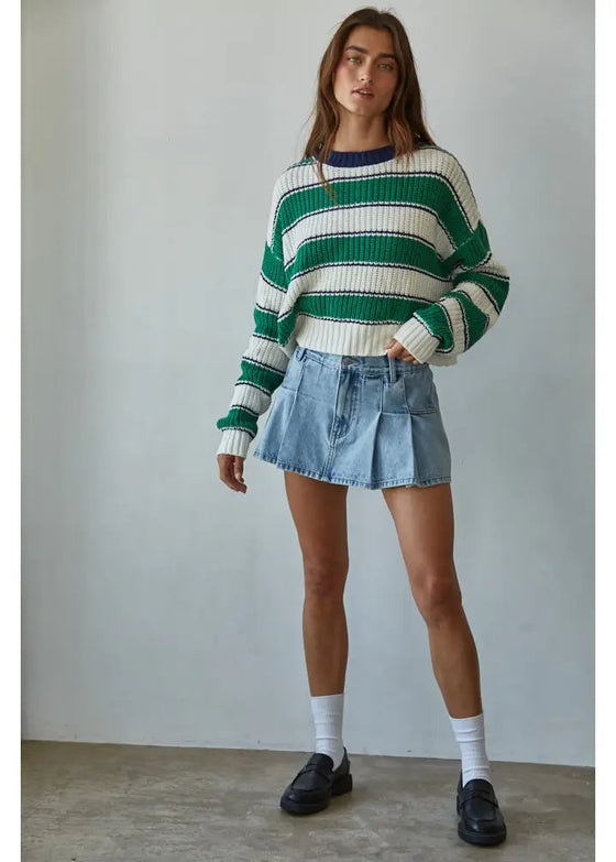 Person wearing a green and white striped sweater with denim shorts against a plain background