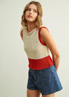 A woman modeling a sleeveless knit top with a cream body and red trim, paired with blue denim shorts, against a plain light gray background.
