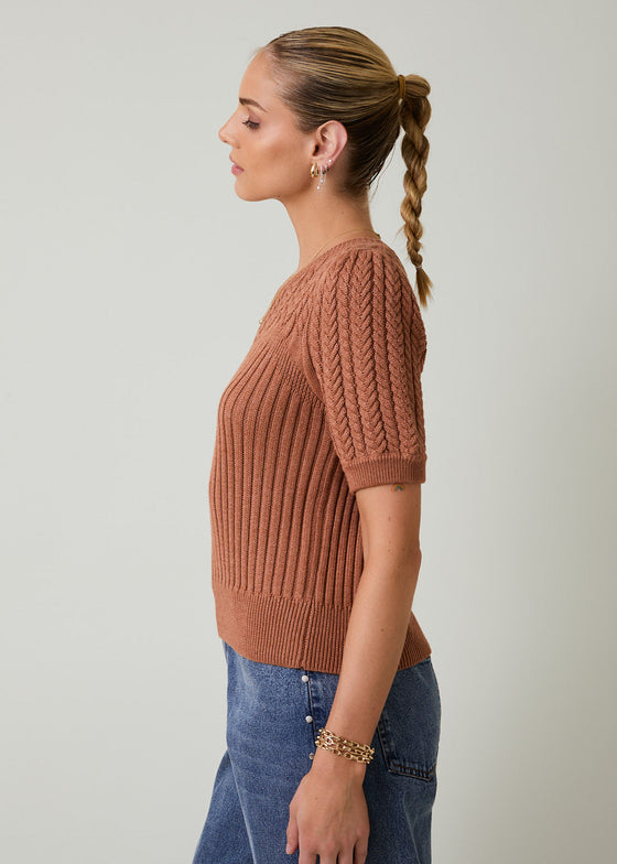 Woman wearing a brown knitted sweater and blue jeans against a plain background