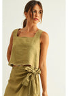Woman wearing a green sleeveless top with a tied skirt against a white background