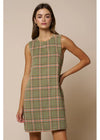 A woman modeling a sleeveless olive green plaid mini dress with thin red and white stripes, set against a solid beige studio background.