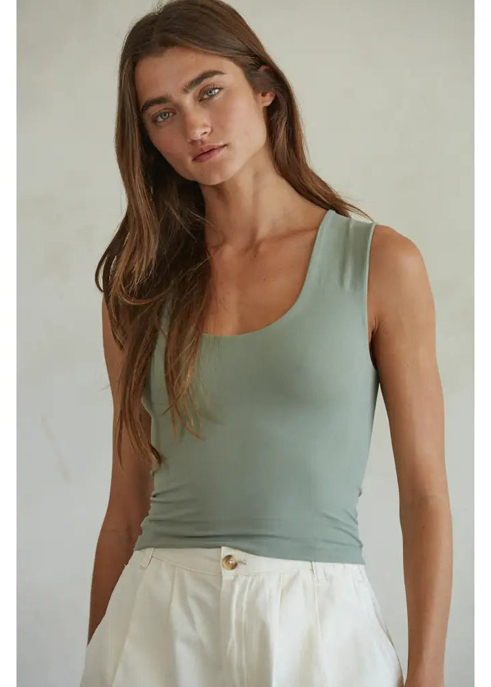  Woman wearing a light green tank top and white pants against a plain background