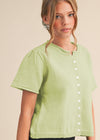 Woman wearing a light green blouse with white buttons on a beige background