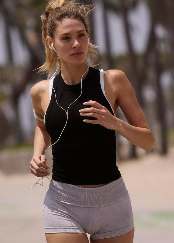 Woman running outdoors with earphones, wearing a black tank top and gray shorts.