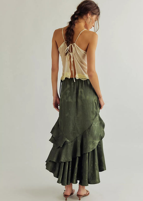 Woman wearing a green ruffled skirt and beige top on a plain background