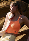 Woman in an orange tank top and white jacket standing against a rocky background