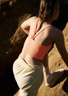 Person wearing an orange sports bra and beige shorts on a dirt path