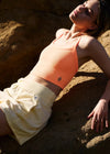 Woman in peach top and beige shorts lying on a rocky surface