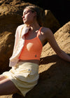 Woman sitting on a rock wearing an orange tank top and light-colored skirt.