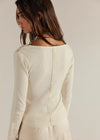 Woman wearing a cream ribbed long-sleeve top against a plain background